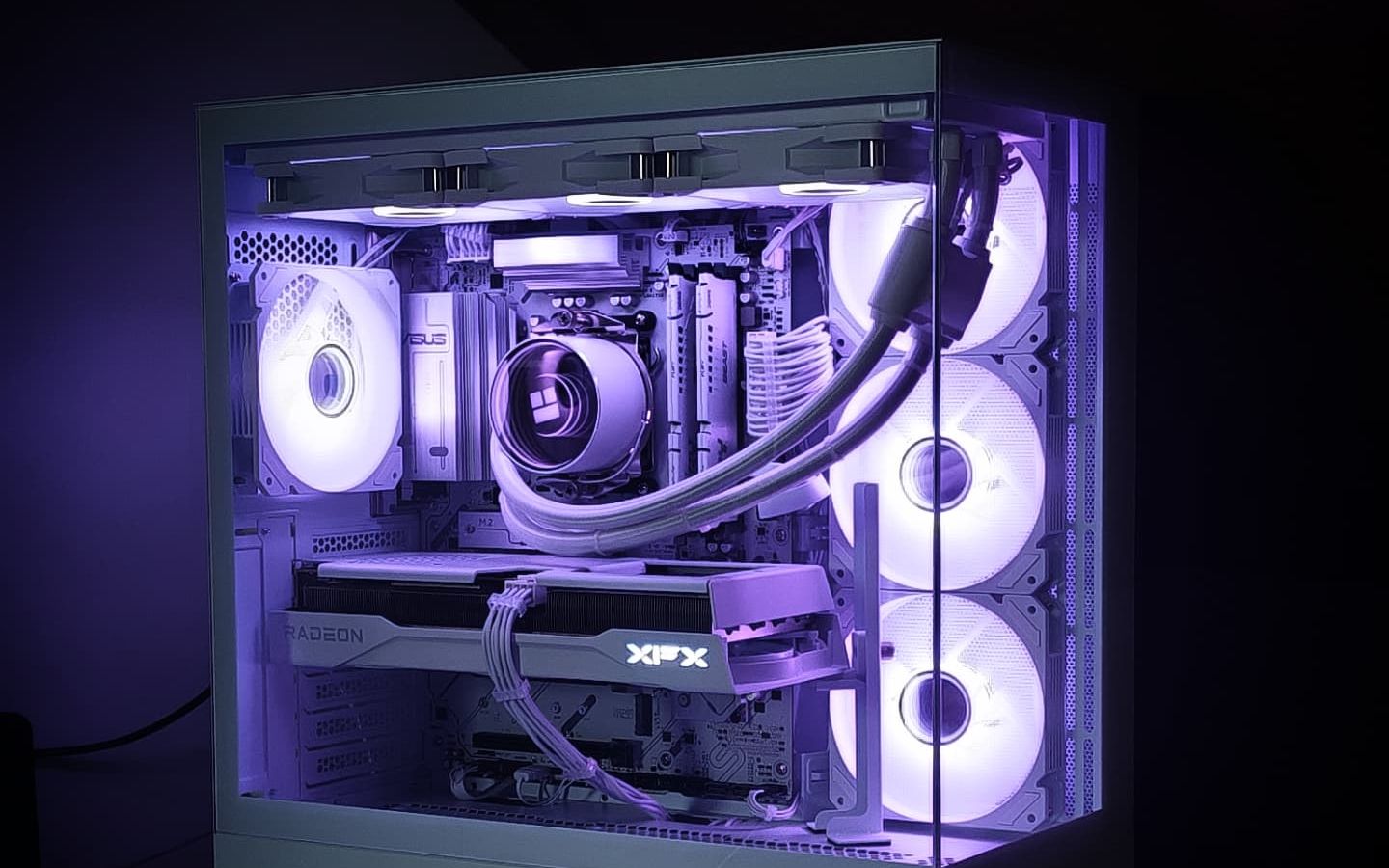 Helemaal witte pc met witte waterkoeling, witte kabels en een XFX Radeon-videokaart, paars verlicht in een donkere kamer