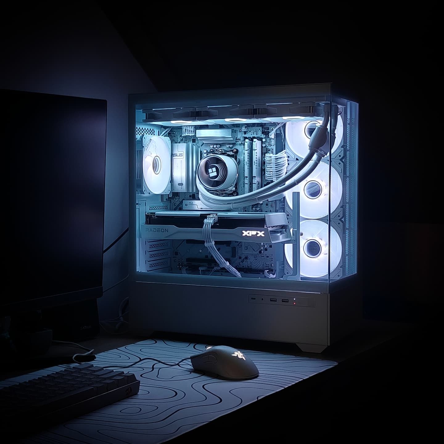 Witte pc met witte waterkoeling en witte kabels in ijsblauw licht, naast toetsenbord en muis